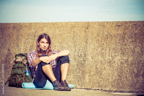 Man tourist backpacker sitting by grunge wall outdoor