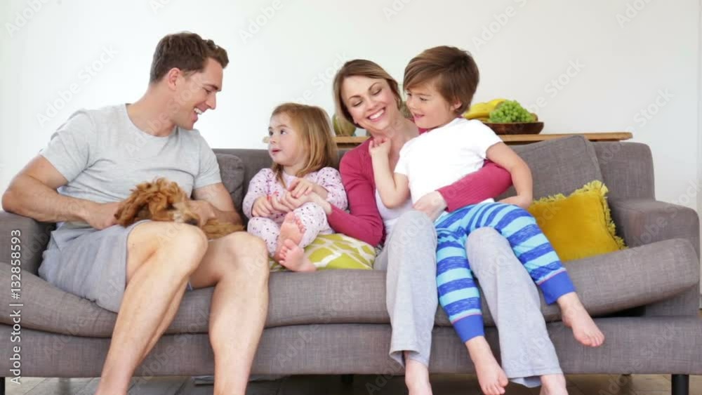 Happy family are sitting together on the sofa in the licing room of their home. They have their dog with them and they are talking and laughing. Happy family are sitting together on the sofa in the licing room of their home. They have their dog with them and they are talking and laughing.
