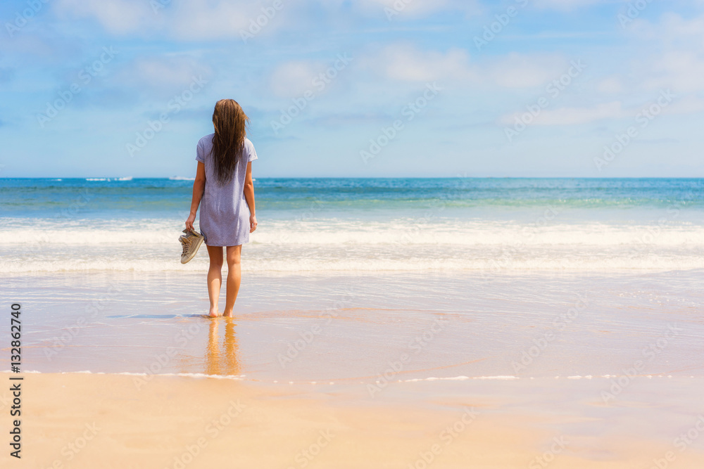 Young girl in dress and shoes in hand standing on beach and looking into sea. Young girl in dress and shoes in hand standing on beach and looking into sea.