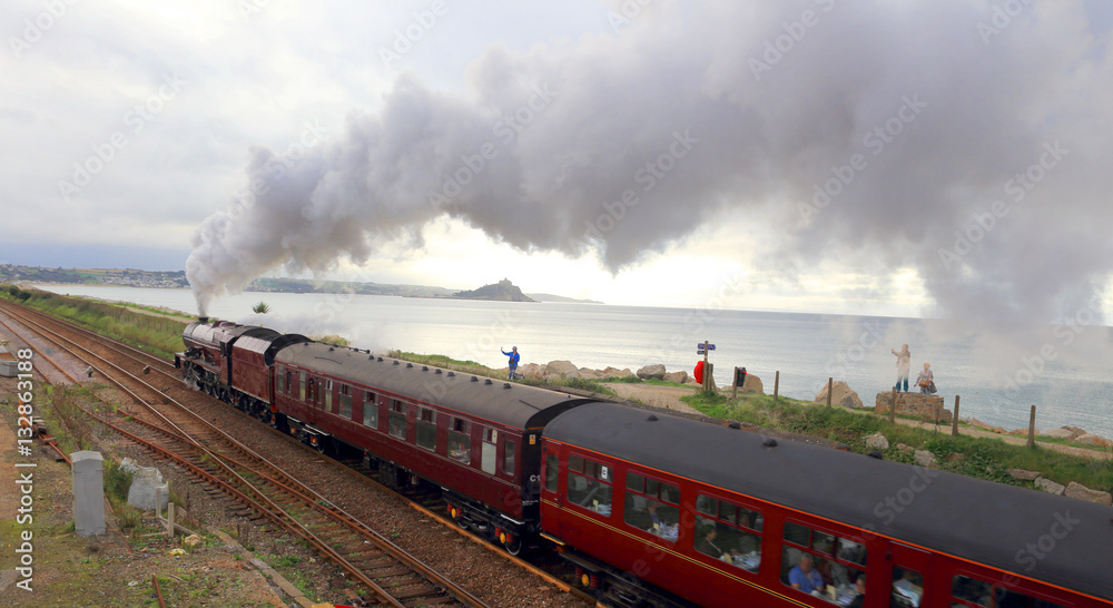 Obraz premium Steam train leaving Penzance, with St Michael's Mount, Mounts Bay, Cornwall, England, UK.