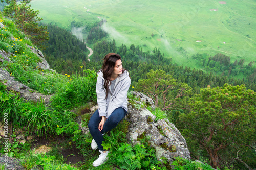 Pretty young woman sitting on mountain top and contemplating lan