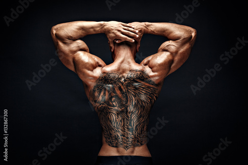 Unrecognizable muscular man with tattoo on back against of black background. Isolated. photo