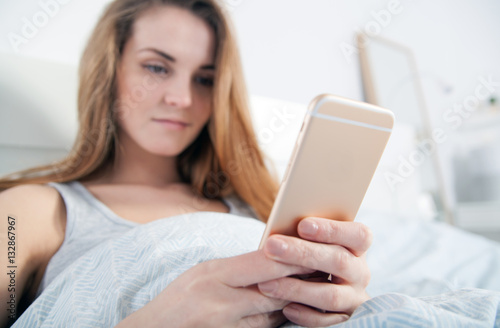 Young woman checking her smartphone lying in bed