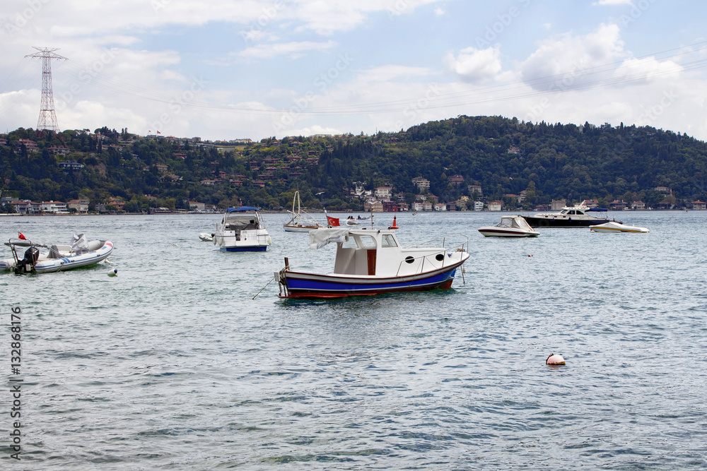 View of bay of luxury neighborhood Bebek on European side of Istanbul. Yachts, fishing boats are parked on Bosphorus. Residential buildings on Asian side are in the background. Cloudy autumn day.