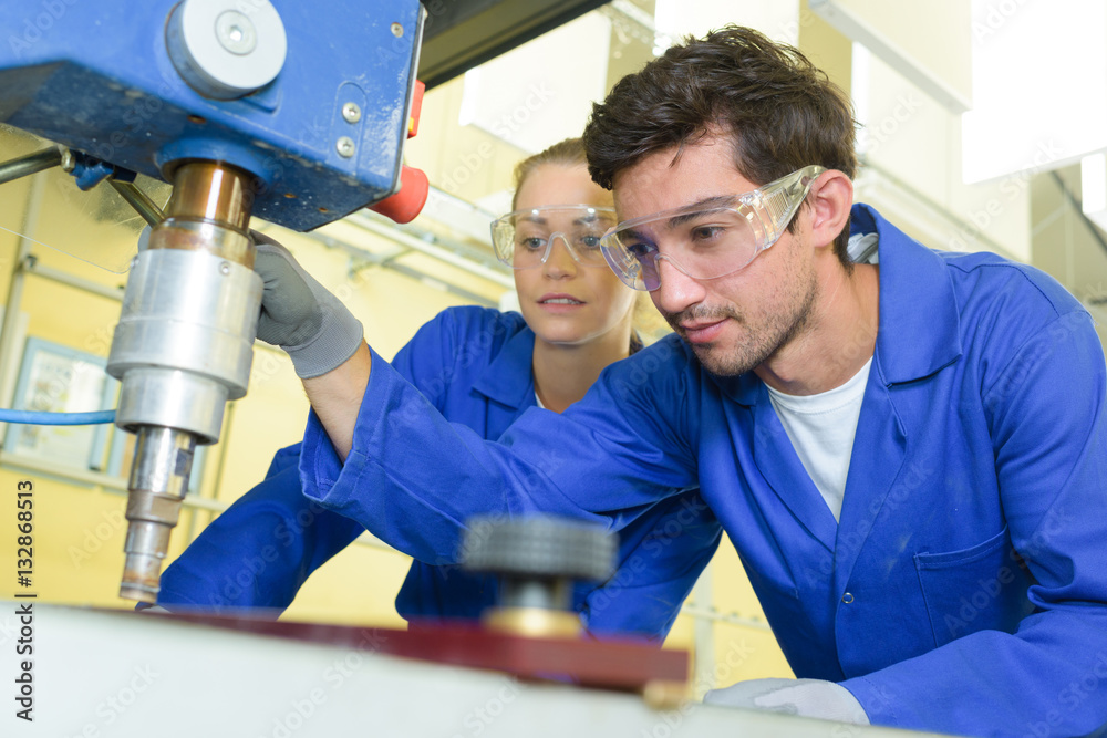 serious trainees focused on drilling metal piece with professional