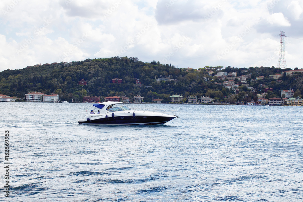Obraz premium Luxury yacht / boat crosses Bosphorus between European and Asian sides in Istanbul. It is cloudy autumn day. It is internationally-significant waterway located in northwestern Turkey