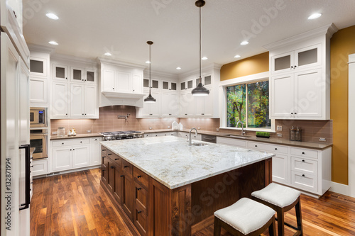Kitchen Interior with Large Island, Sink, White Cabinets, Pendant Lights, and Hardwood Floors in New Luxury Home