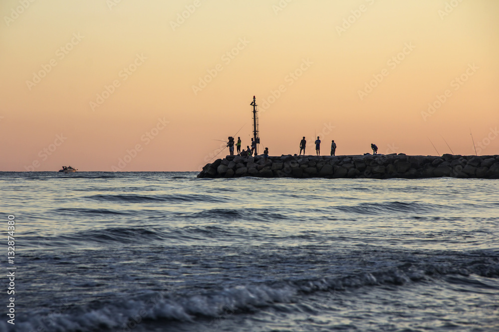 Sunset on Tyrrhenian sea, view of breakwater, fishermen silhouettes, harbor and seacoast of Terracina, Lazio, Italy