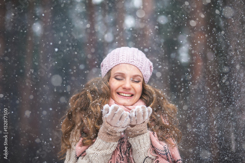 Girl wearing warm winter clothes and hat play ,smile and blowing snow in the winter forest
