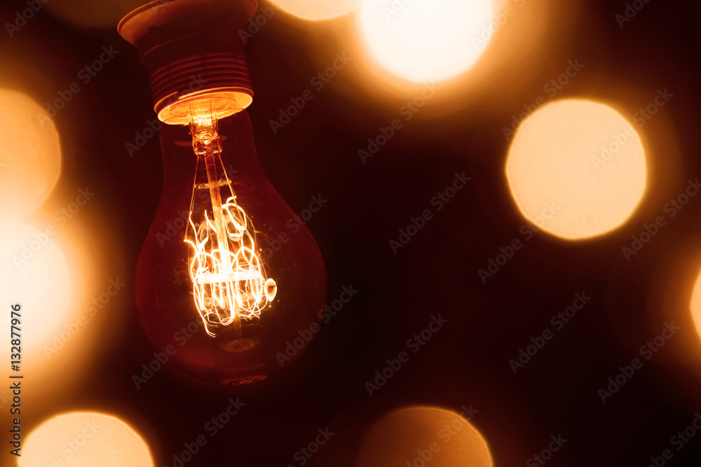 lighted vintage incandescent bulb on dark orange  blurred background