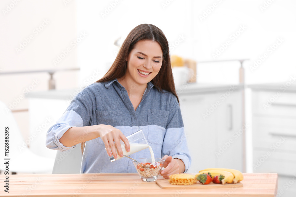 Young woman pouring milk into bowl with breakfast Young woman pouring milk into bowl with breakfast