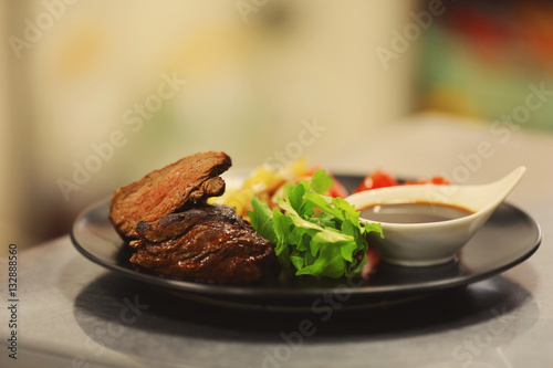 Plate with tasty meat, fried vegetables and sauce on table in restaurant, close up