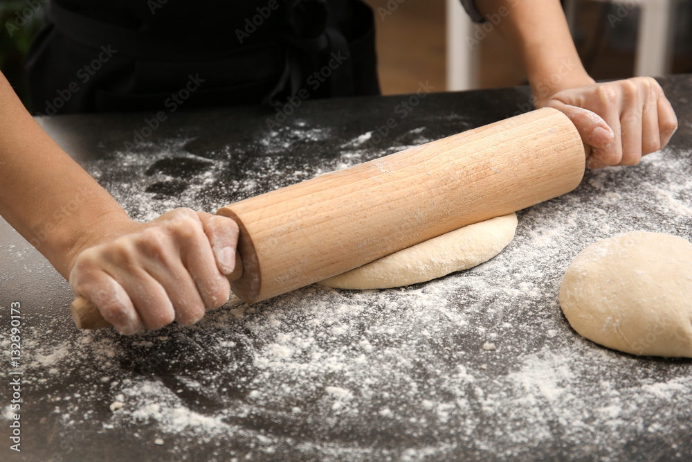 Young woman rolling out dough in kitchen