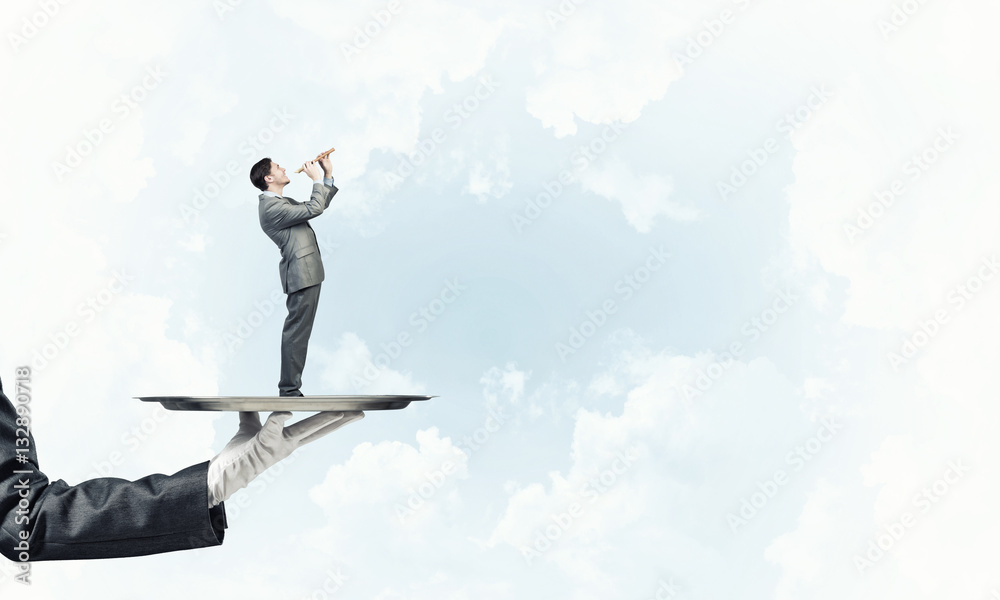 Businessman on metal tray playing fife against blue sky background Businessman on metal tray playing fife against blue sky background