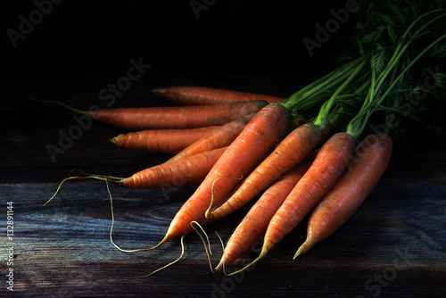 Fresh orange carrots with green leaves on dark rustic wood, black background