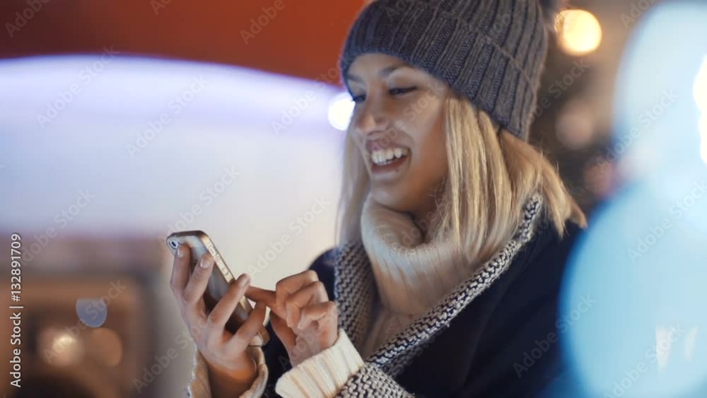 Woman using smartphone in a city at night. Girl enjoying winter holiday season. Concept of  social networking, communicating, using app. Christmas bokeh lights on background.