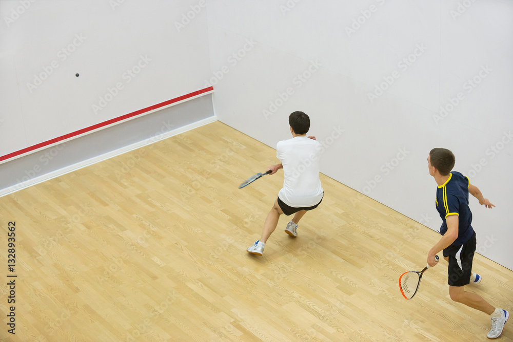 Squash players in action on squash court, back view/Two men playing match of squash