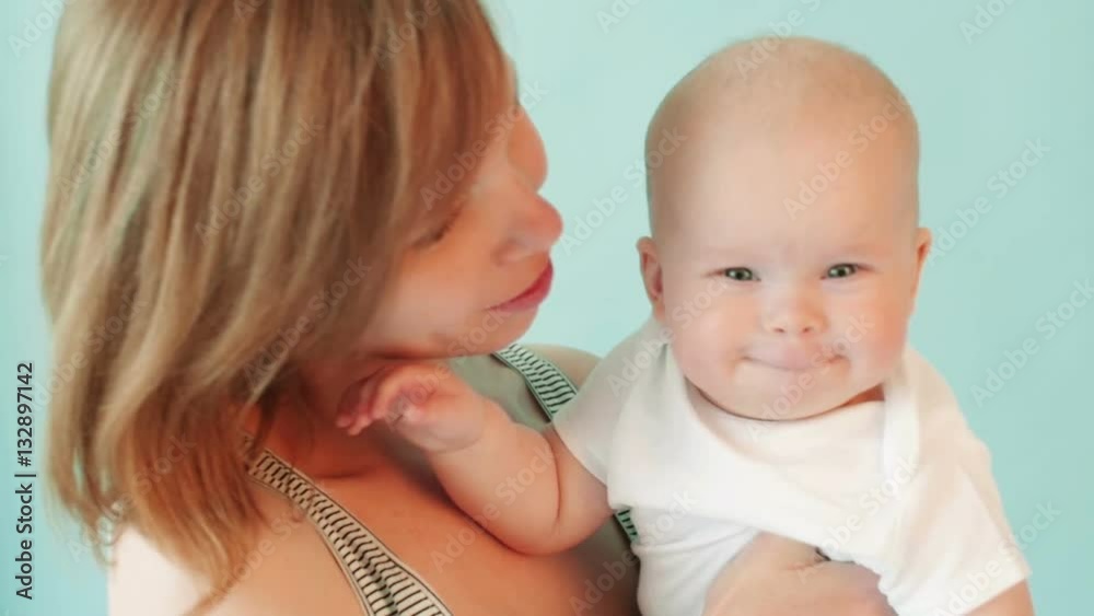 Young white woman holds her child on the hands and kisses him on the cheek. Young white woman holds her child on the hands and kisses him on the cheek.