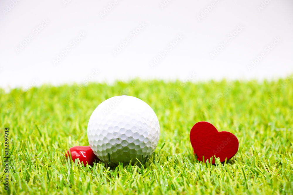 Naklejka premium golf ball and red heart are on green grass
