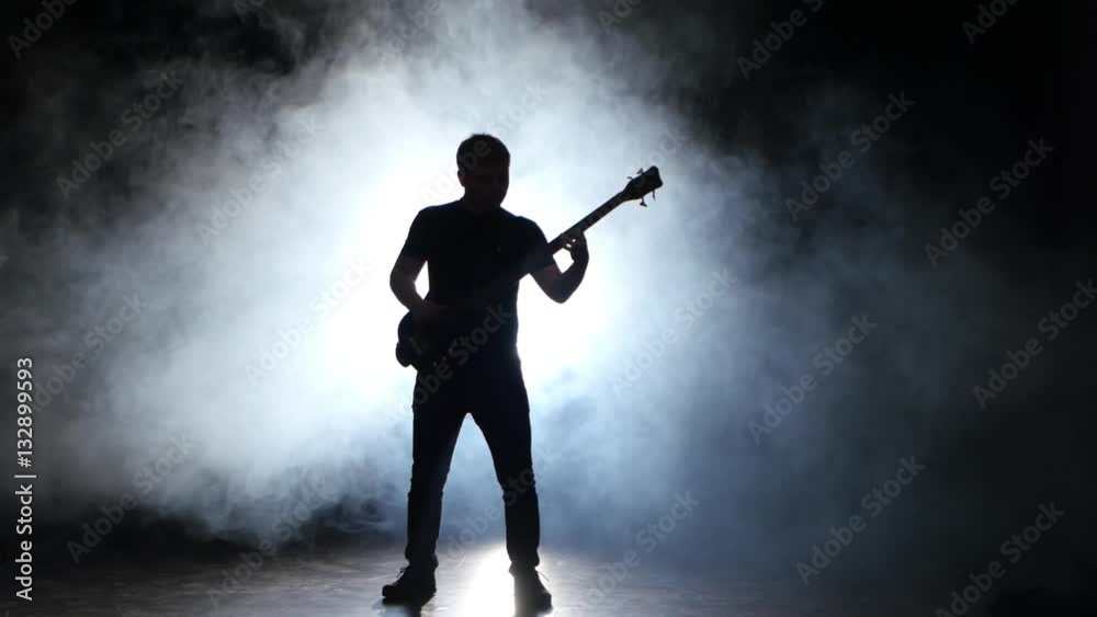 Musician jump while playing the bass guitar. Dark with smoke