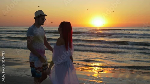 Couple of young man and woman meeting on a sandy beach and kissing with passion at sunrise