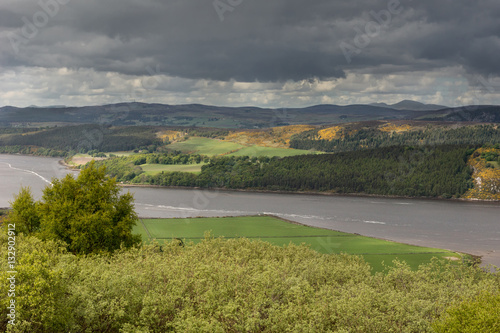 Dornoch Firth, Scotland - June 3, 2012: Panorama of a stretch of the Firth, bordered on both sides by green landscape. All under menacing dark clouds. Some sun spots light up part of the terrain.