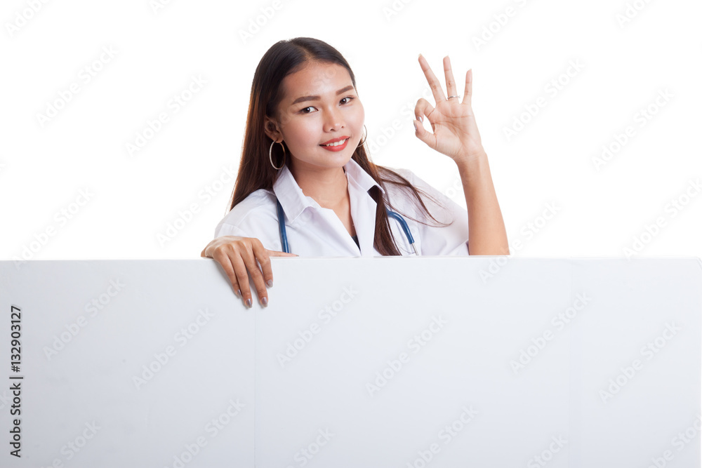 Young Asian female doctor show OK sign behind blank white billb Young Asian female doctor show OK sign behind blank white billb