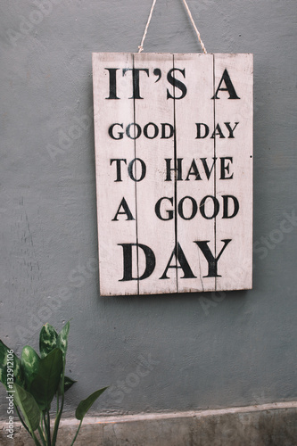 Vintage wooden board with motivational phrase hanging on the grey wall.  Phrase - it's a good day to have a good day.