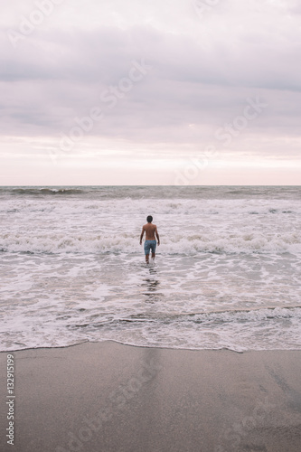Man stands in the ocean during sunrise in a white fiam, Indonesia, Bali photo