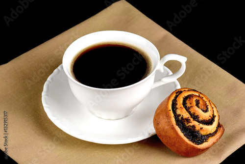 Cup of coffee a bun with poppy seeds on a black background