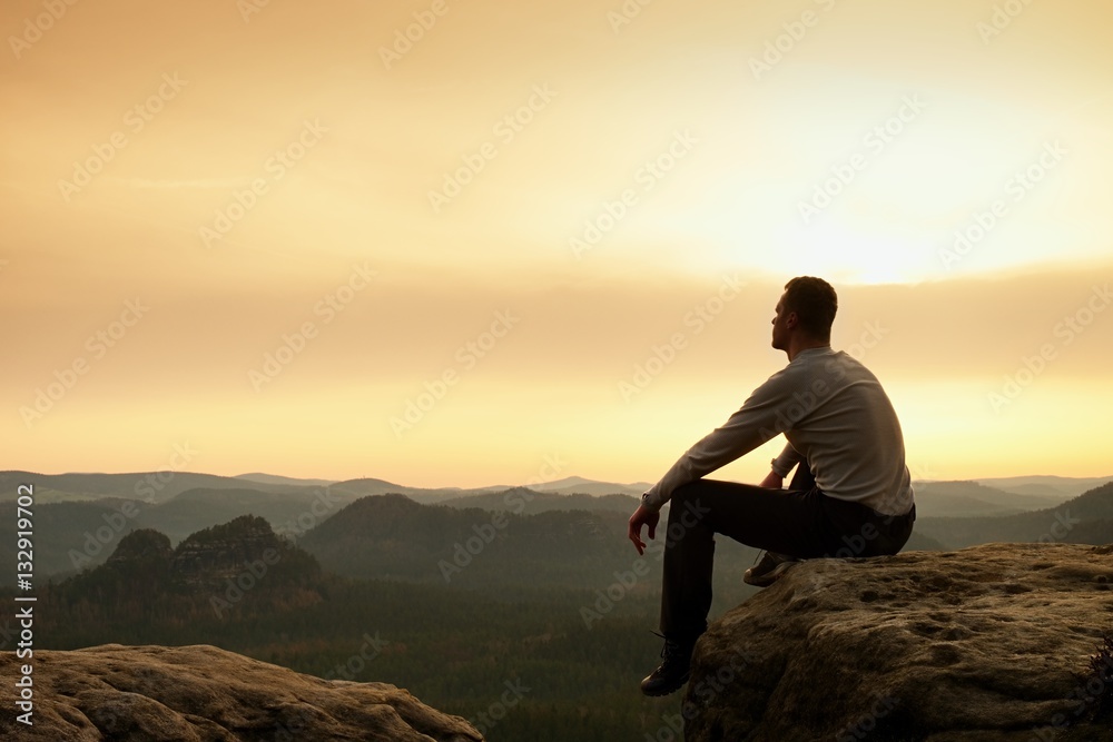 Adult hiker in black sit on mountain  edge. Man enjoying evening