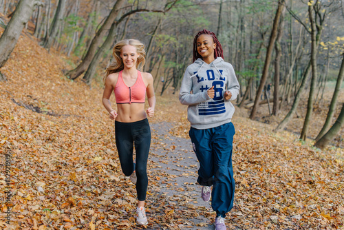 Happy attractive women running in autamn park. Blonde and african girls have training in the morning. Golden leaves around photo