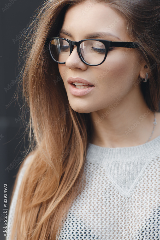 Young beautiful woman with model looks,wears black-rimmed glasses,beautiful makeup,long red hair,big black eye lashes,wearing a light knitted sweater posing in Studio on dark gray background Young beautiful woman with model looks,wears black-rimmed glasses,beautiful makeup,long red hair,big black eye lashes,wearing a light knitted sweater posing in Studio on dark gray background