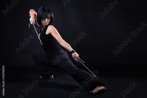 young woman in fighting stance holding a pair of sai: studio portrait on black background