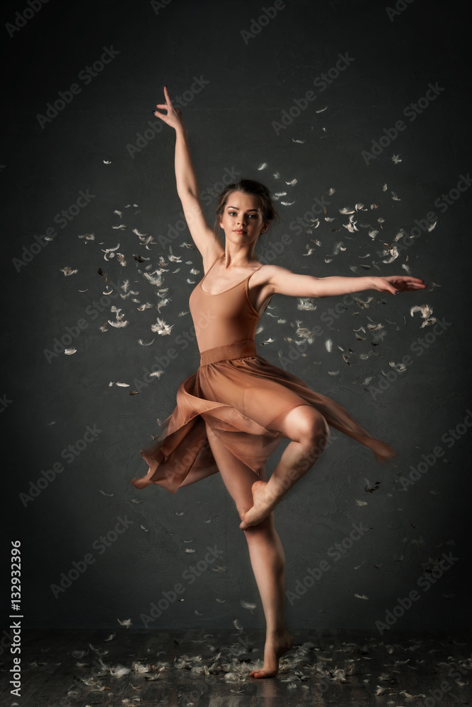 girl dancing barefoot with feathers. ballet. grey background

