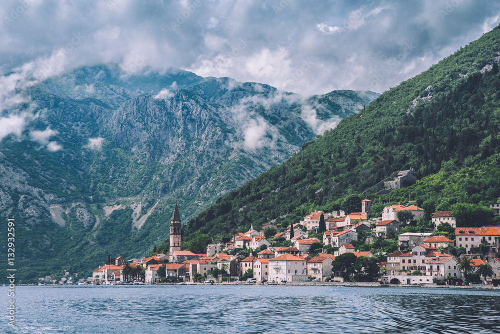 Famous ancient Perast village on Kotor bay by cloudy day in Montenegro. View to Perast Old Town roofs and mountains from water of Boka Kotorska. Postcard montenegrin landscape.