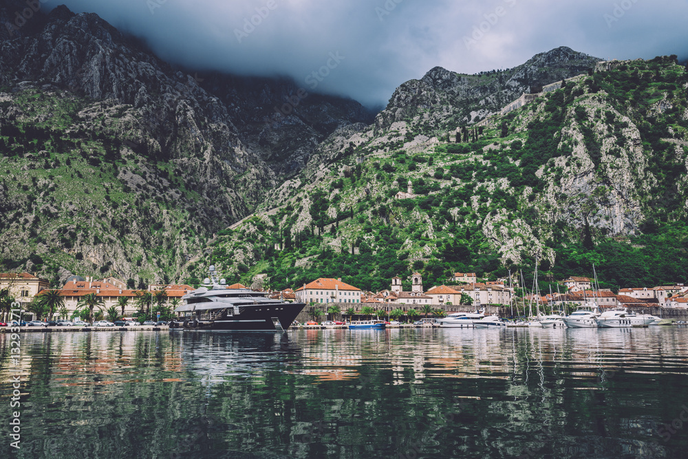 June 3th, 2016 - Kotor, Montenegro. Famous ancient Kotor City on Kotor bay by cloudy day in Montenegro. View to Kotor Old Town roofs, mountains and boats reflected on water of Boka Kotorska.