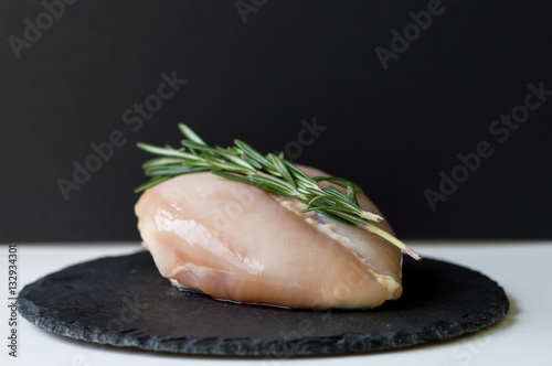 Fresh chicken breast with fresh aromatic rosemary leaves on black slate board. Black background