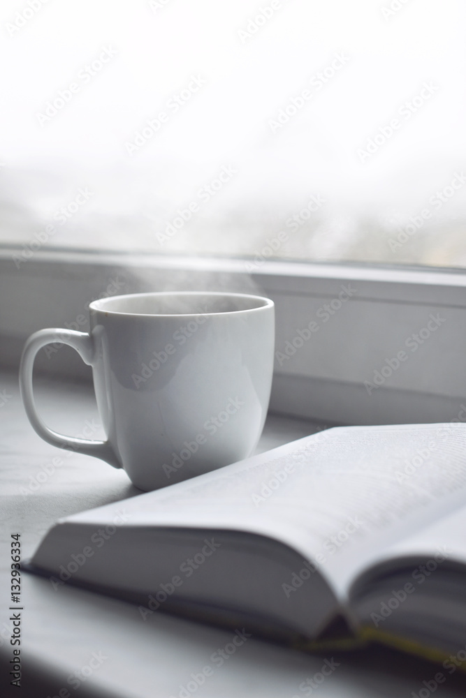 Cozy home still life: cup of hot coffee and opened book on windowsill against snow landscape outside. Winter holidays, Christmas time concept, free copy space Cozy home still life: cup of hot coffee and opened book on windowsill against snow landscape outside. Winter holidays, Christmas time concept, free copy space