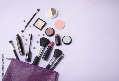 Fototapeta Naklejka Na Ścianę i Meble -  A purple leather make up bag, with cosmetic beauty products spilling out on to a pastel colored background, with blank space at side