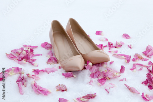 Pair of nude women heels shoes on snow with rose petals. Winter scene. Fashion ideas. Christmas, wedding and Valentines day background. 