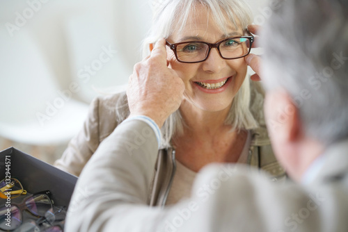Senior woman in optical store trying eyeglasses on