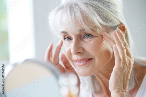 Fototapeta Portrait of senior woman applying anti-aging cream