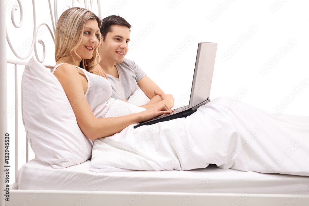 Happy young couple lying in bed and looking at a laptop
