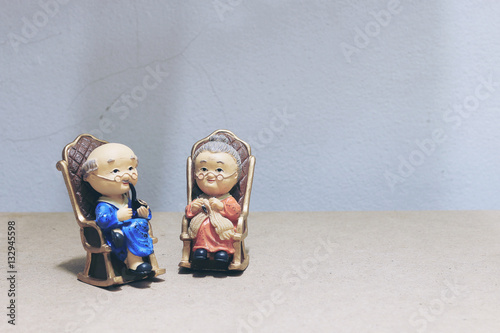 still life photography with lovely Grandpa is smoking and Grandma with cat doll siting rocking bamboo chair with low light from the window in the dark on wood background. photo