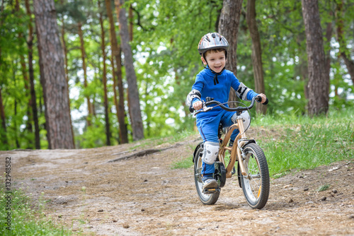 Happy funny little kid boy in colorful raincoat riding his first bike on cold day in forest. Active leisure for children outdoors. carefree childhood concept