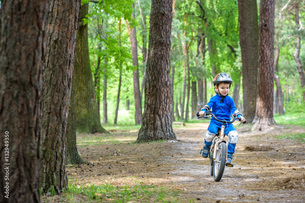 Obraz premium Happy cute blond kid boy having fun his first bike on sunny summer day, outdoors. child making sports. Active leisure for children. wear safety helmet. is smiling and cicling