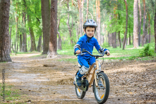 Happy kid boy of 4 years having fun in autumn or summer forest with a bicycle on beautiful fall spring day. Active child making sports. Safety, , leisure kids concept.
