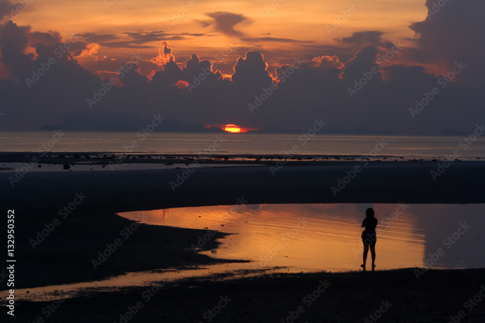 The girl walked on the beach with sunset background. 