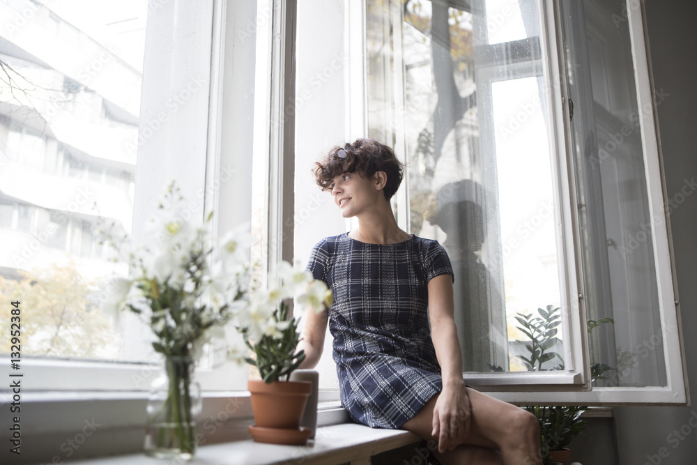 Young woman sitting on window sill at home Young woman sitting on window sill at home